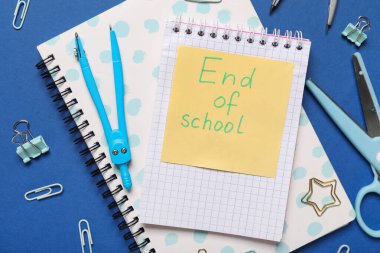 Okulun Sonu yazılı kağıt, mavi arkaplanda not defterleri ve ataçlar. Yakın çekim.