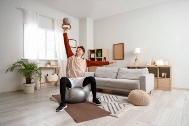 Kettlebell antrenmanıyla evde spor yapan genç adam.