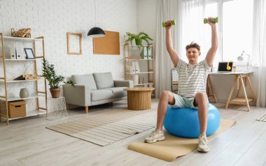 Dambılı genç adam evde fitbol antrenmanı yapıyor.