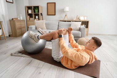 Sportif genç adam evde karın kası yapıyor.