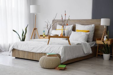 İçinde ağaç dalları ve vazolarda Paskalya yumurtaları olan hafif yatak odasının içi.