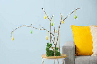 İçinde ağaç dalları olan vazolar, Paskalya yumurtaları ve oyuncak tavşanlar oturma odasındaki mavi duvarın yanında.