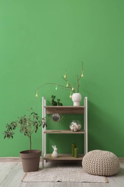 Ağaç dalları olan vazolar, paskalya yumurtaları ve odanın yeşil duvarının yanında raflarda duran tavşanlar.