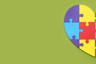 Yeşil arka planda renk yapbozundan yapılmış bir kalp. Otistik bozukluk kavramı