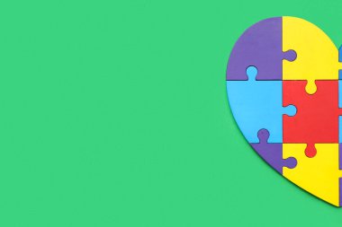 Yeşil arka planda renk yapbozundan yapılmış bir kalp. Otistik bozukluk kavramı