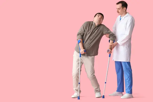 Young man with crutches and doctor on pink background. National Cerebral Palsy Awareness Month