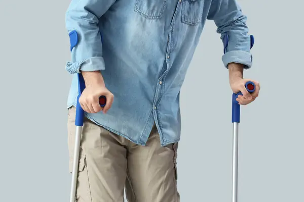Young man with crutches on light background. National Cerebral Palsy Awareness Month