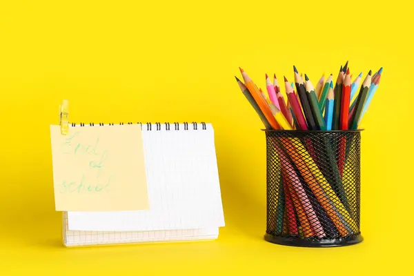 Paper with text END OF SCHOOL and pencil holder full of colorful pencils  on yellow background