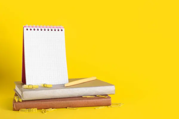 Books and notebook with pen on yellow background. End of school