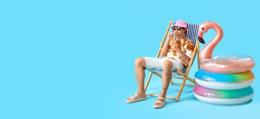 Genç adam güverte sandalyesinde dinlenirken kokteyl içiyor açık mavi arka planda mesaj için yer var.