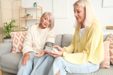 Olgun bir kadın, evinde arkadaşının tansiyonunu ölçüyor.