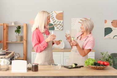Salatalıklı olgun bayan arkadaşlar mutfakta şarap içiyorlar.