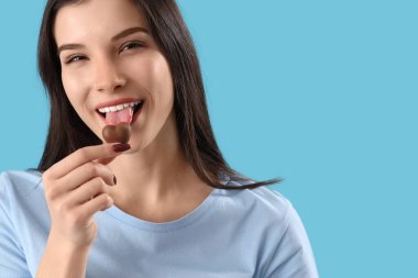 Mavi arka planda kalp şeklinde çikolata yiyen genç kadın, yakın plan.