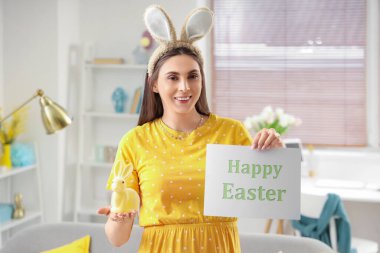 Tavşan kulaklı genç bir kadın elinde kağıdıyla Mutlu Paskalyalar ve evde tavşan