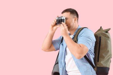 Sırt çantası ve fotoğraf makinesi olan erkek turist pembe arka planda bir şeyin fotoğrafını çekiyor.