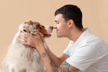 Bej arka planda Avustralya çoban köpeğine sarılan genç adam, yakın plan.