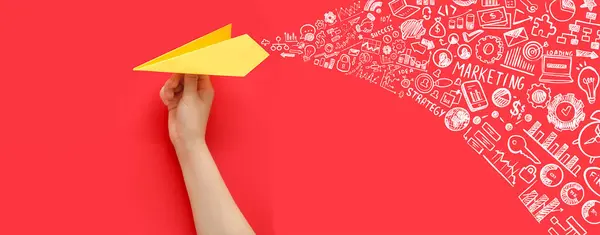 Hand with paper plane and drawn icons on red background. Concept of marketing strategy
