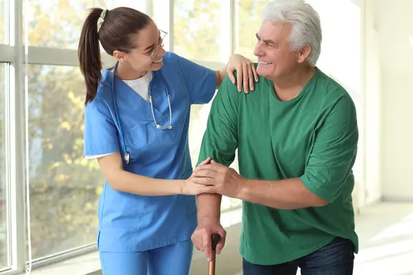 Nurse helping senior man with stick to walk at hospital