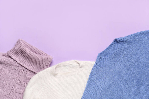 Set of warm female sweaters on lilac background, closeup