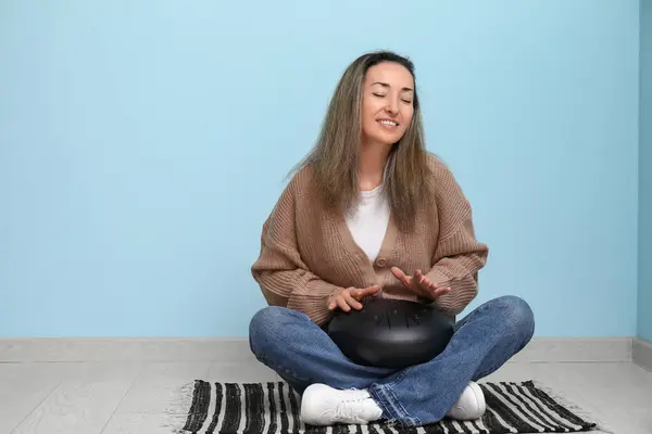 stock image Beautiful mature woman with glucophone sitting on floor near blue wall