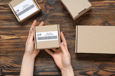 Ahşap masada üzerinde etiket ve barkod olan küçük bir karton paket taşıyan kadın.