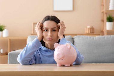 Evde kumbarası olan stresli genç bir kadın.