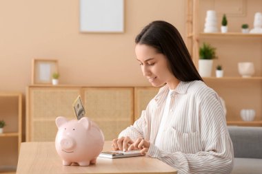 Evde hesap makinesi ve kumbarası olan genç ve güzel bir kadın.