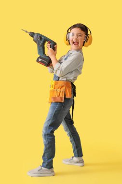 Sarı arka planda matkabı olan şirin bir inşaatçı.