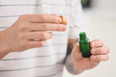 Mutfakta bir şişe CBD yağı olan genç adam, yakın plan.