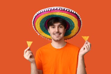 Sombrero ve turuncu arka planda tortilla cipsi olan genç bir adamın portresi. Ulusal Tortilla Cipsi Günü kutlaması