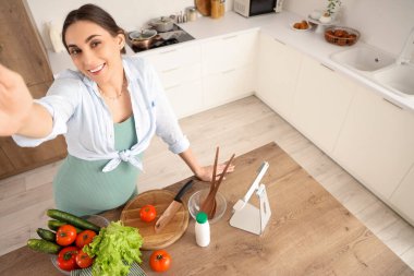 Taze sebzeli genç hamile kadın mutfakta selfie çekiyor.