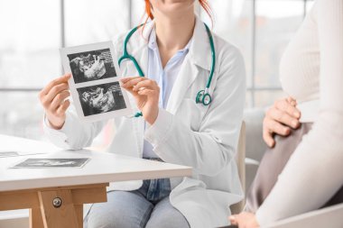 Kadın doktor klinikte hamile kadın ultrason görüntüsü gösteriyor.