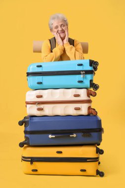 Sarı arka planda bavulları olan yaşlı bir bayan turist.