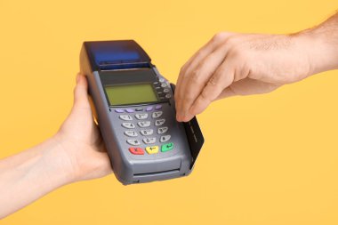 Sarı arka planda kredi kartı ve ödeme terminali olan bir erkek.