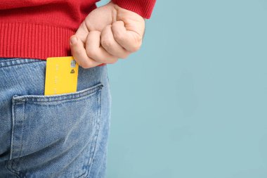Genç adam kredi kartını mavi arka planda kot pantolonun cebine koyuyor, yakın plan.