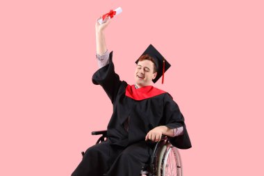 Pembe arka planda diploması olan tekerlekli sandalyede mutlu bir erkek mezun.