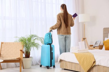 Otel odasının penceresinin yanında çantalı ve pasaportlu bir kadın turist.
