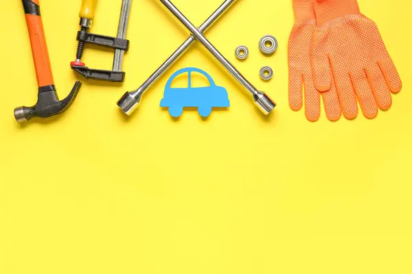 Set of mechanic tools, paper car and gloves on yellow background. Mechanic concept
