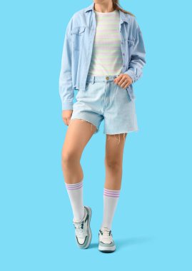 Mavi arka planda kot şortlu genç kadın.