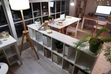 Ofis içi masalar, raf ünitesi ve geceleri parlayan lambalar.