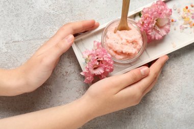 Kadın eli, bir kase vücut fırçası ve arka planda güzel çiçekler, yakın plan.