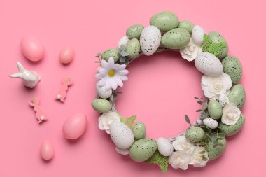 Beyaz çiçekli Paskalya çelengi, yumurtalar, kelebekler ve pembe arka planda tavşan heykelciği