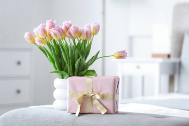 Uluslararası Kadınlar Günü için laleli vazo ve hediye kutusu yatak odasındaki yumuşak bankta, yakın plan.