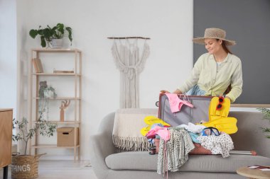 Evdeki kanepede içi yaz eşyalarıyla dolu valiziyle bir kadın turist.