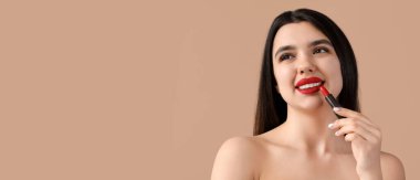 Bej arkaplana kırmızı ruj sürerken mutlu genç kadın metin için boşluk bırakıyor