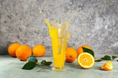 Gri arka planda taze meyveler ve sıçramalı bir bardak lezzetli portakal suyu.