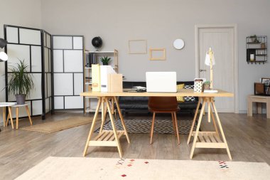 Modern ofis, ahşap masa, dizüstü bilgisayar, masa lambası ve siyah kanepe.