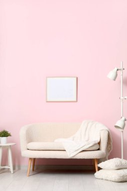 Sıcak beyaz kanepe, yastıklar ve pembe duvarın yanındaki lamba.