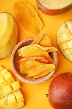 Turuncu arka planda kurutulmuş mango dilimleri olan ahşap kase.