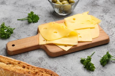 Lezzetli peynir dilimleri, maydanozlu ve hafif arka planda zeytinli pano, yakın plan.